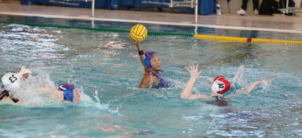 一名水球运动员举着一个黄色的球，其他运动员在她周围泼水.